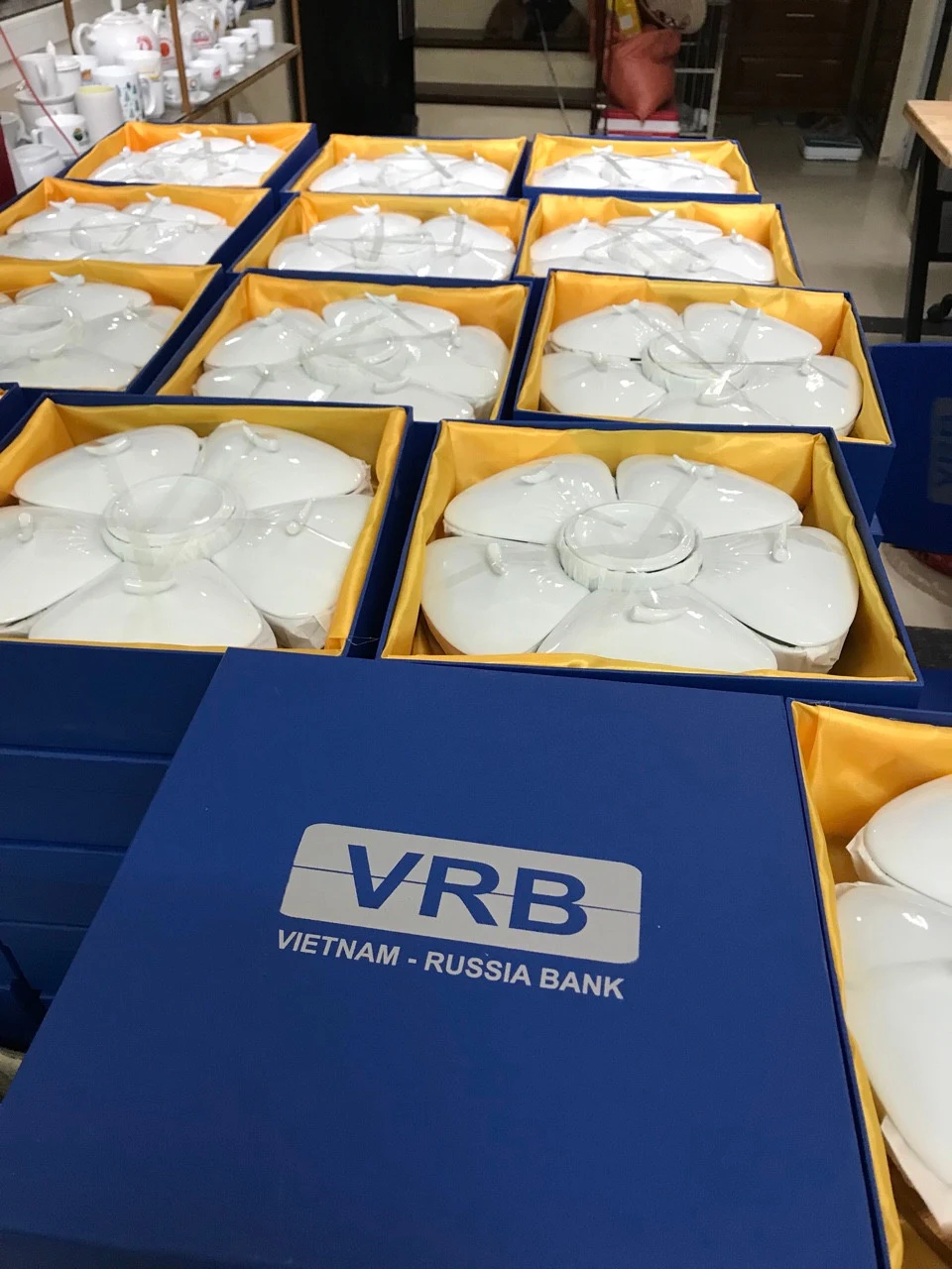 Nhiều bộ gốm sứ trắng trong hộp xanh c&oacute; lớp l&oacute;t v&agrave;ng, nắp một hộp in VRB