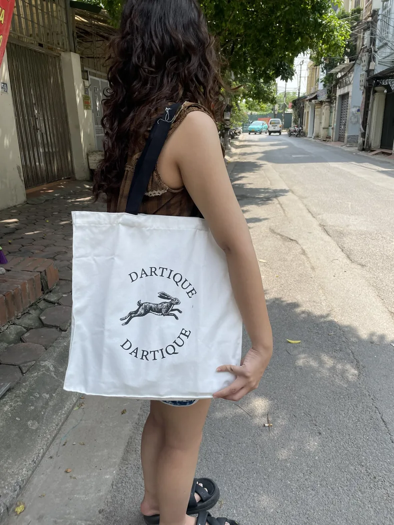 Người d&ugrave;ng đeo t&uacute;i canvas trắng c&oacute; biểu trưng v&agrave; h&igrave;nh in trong bối cảnh đường phố