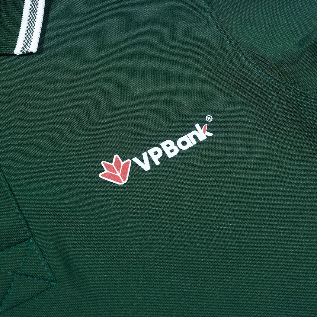 Logo in tr&ecirc;n ngực &aacute;o polo xanh nằm c&aacute;ch đường viền cổ v&agrave; đường may