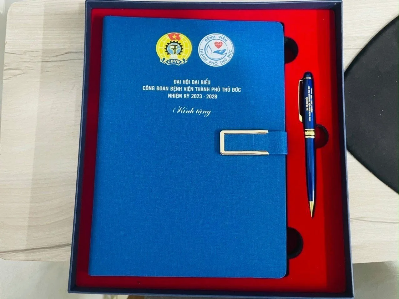 Sổ b&igrave;a xanh in logo kh&aacute;ch h&agrave;ng v&agrave; b&uacute;t c&ugrave;ng đặt trong khay l&oacute;t đỏ của hộp qu&agrave;
