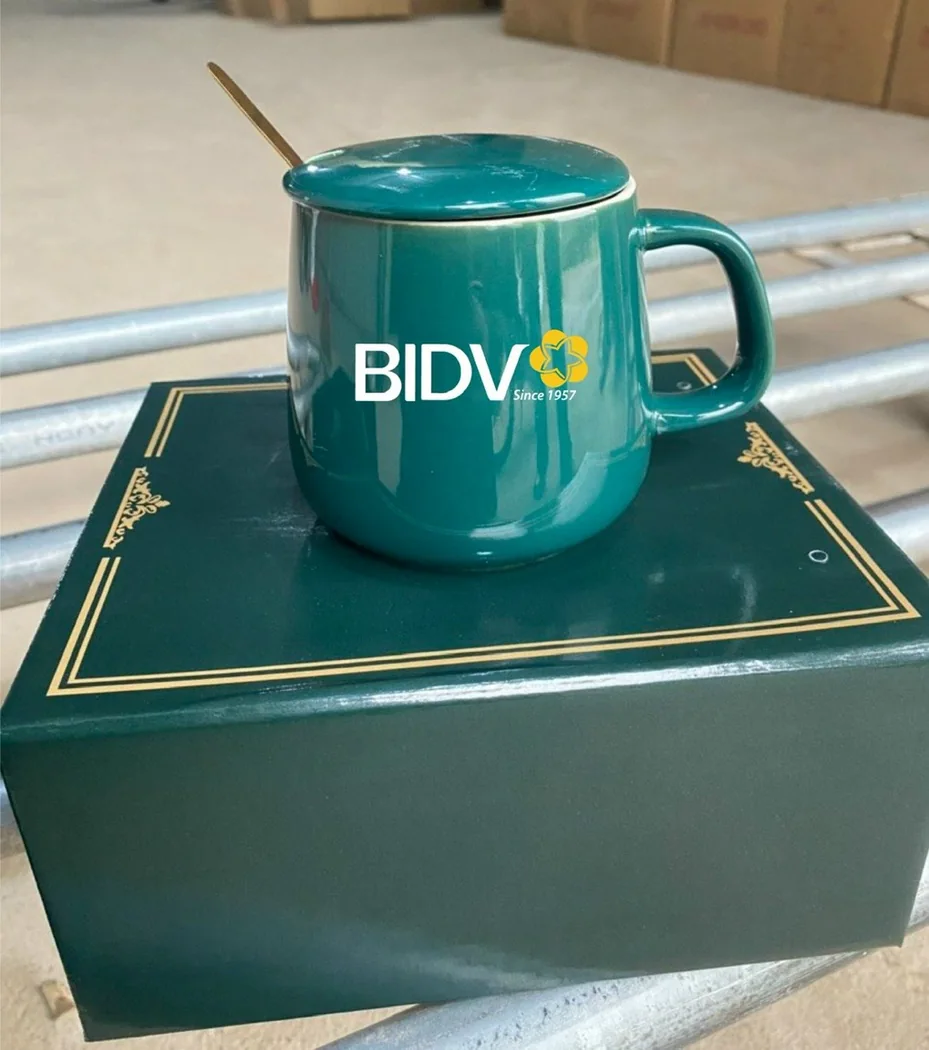 Cốc sứ xanh c&oacute; quai, nắp v&agrave; logo BIDV in tr&ecirc;n th&acirc;n đặt c&ugrave;ng hộp qu&agrave;
