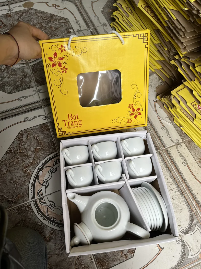 S&aacute;u ch&eacute;n v&agrave; ấm sứ nằm trong c&aacute;c &ocirc; carton t&aacute;ch biệt, cạnh nhiều vỏ hộp c&ugrave;ng mẫu