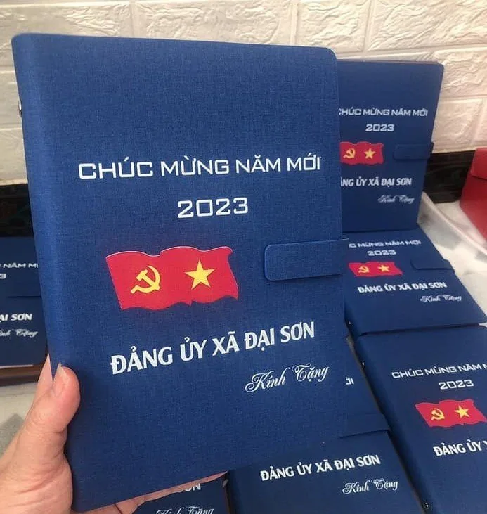 Tay cầm một sổ da xanh in nội dung b&ecirc;n cạnh nhiều sổ c&ugrave;ng mẫu