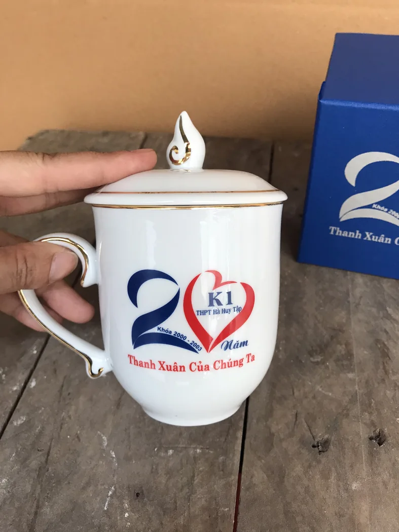 Cốc sứ c&oacute; nắp in logo được cầm để quan s&aacute;t b&ecirc;n ngo&agrave;i