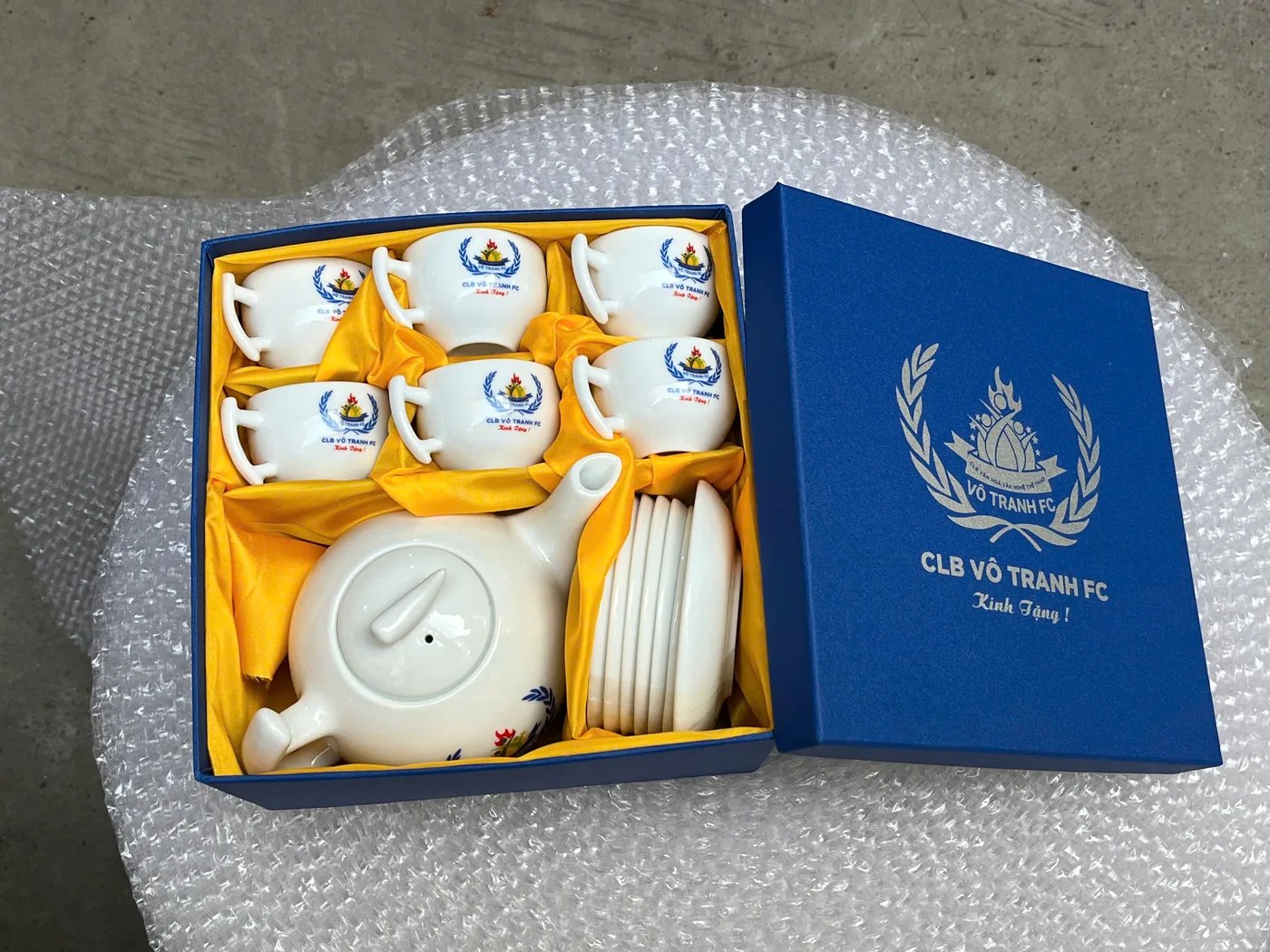 Bộ ấm chén in logo xếp trong hộp xanh với phần lót giữ từng món