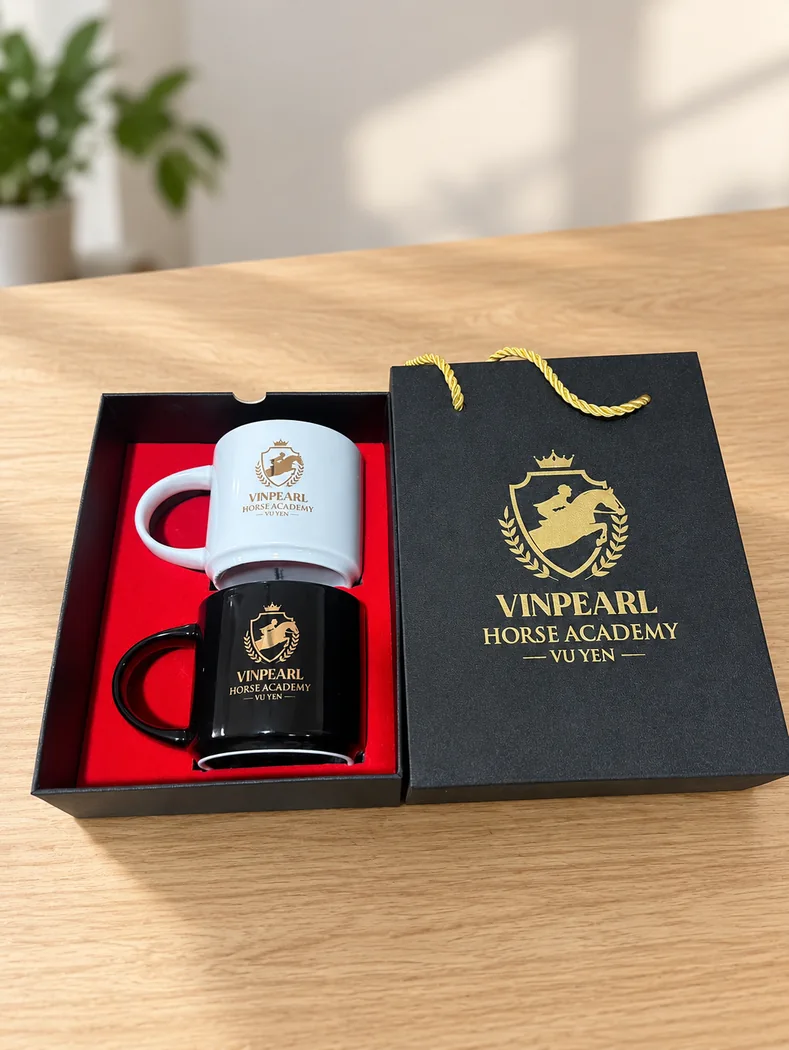 Bộ hai cốc trắng đen v&agrave; t&uacute;i c&ugrave;ng in Vinpearl Horse Academy, đặt tr&ecirc;n b&agrave;n sau chỉnh bối cảnh bằng AI