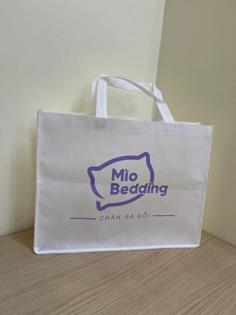 T&uacute;i vải kh&ocirc;ng dệt m&agrave;u trắng c&oacute; quai, nẹp m&eacute;p v&agrave; logo kh&aacute;ch h&agrave;ng m&agrave;u t&iacute;m