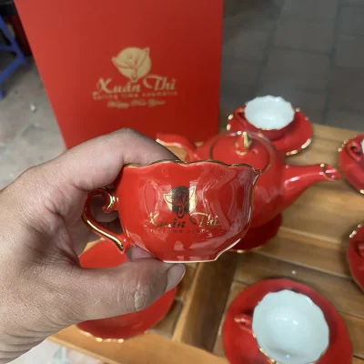 Ảnh thật chén đỏ miệng cánh hoa lòng trắng với logo in vàng có phản sáng