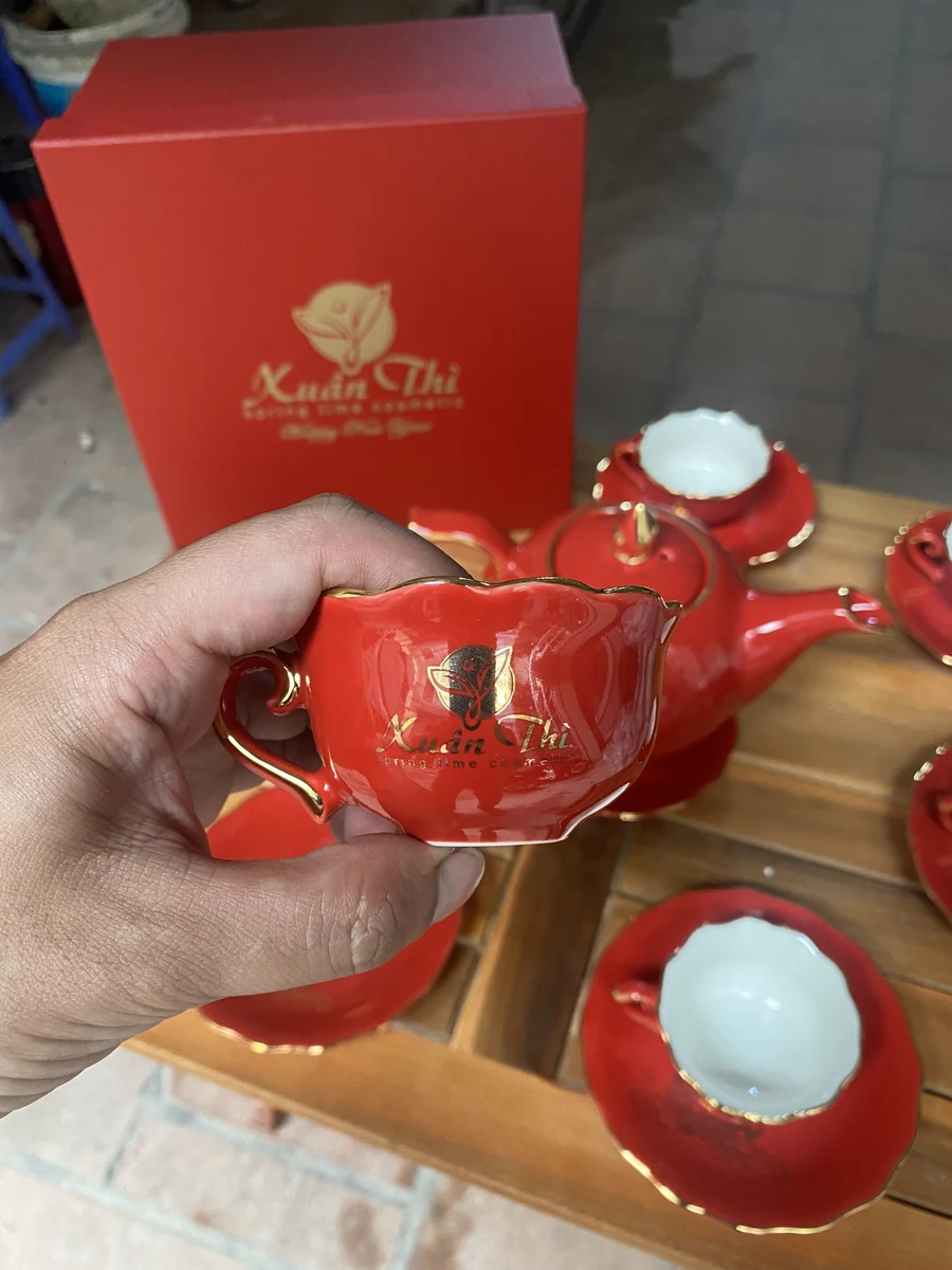 Ảnh thật chén đỏ miệng cánh hoa lòng trắng với logo in vàng có phản sáng