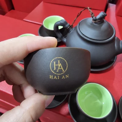 Demo logo HA Hai An nhỏ in vàng trên chén tử sa nâu cầm tay