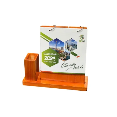Lịch để bàn gỗ nâu cam kèm hộp bút bên trái – xem hai vòng treo giấy và phần gỗ lộ phía dưới